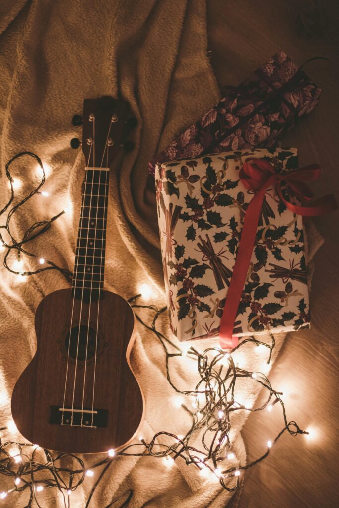 Warm holiday scene featuring a ukulele and festive gift surrounded by fairy lights.
